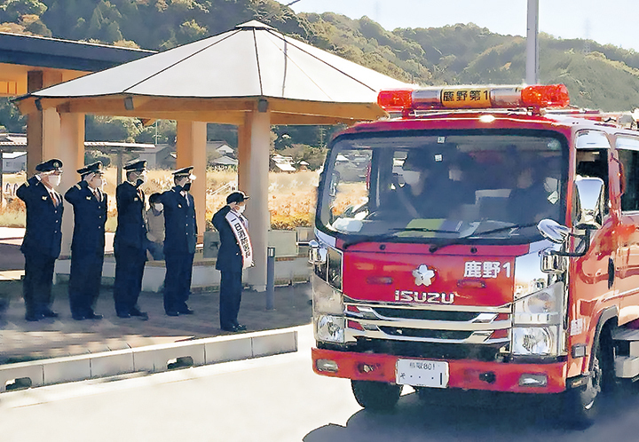 消防車に乗車している消防団員と車外で敬礼している複数名の消防団員