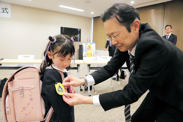 市役所で交通事故防止の黄色いワッペンをワッペンを付けてもらっている新1年生代表5名の様子